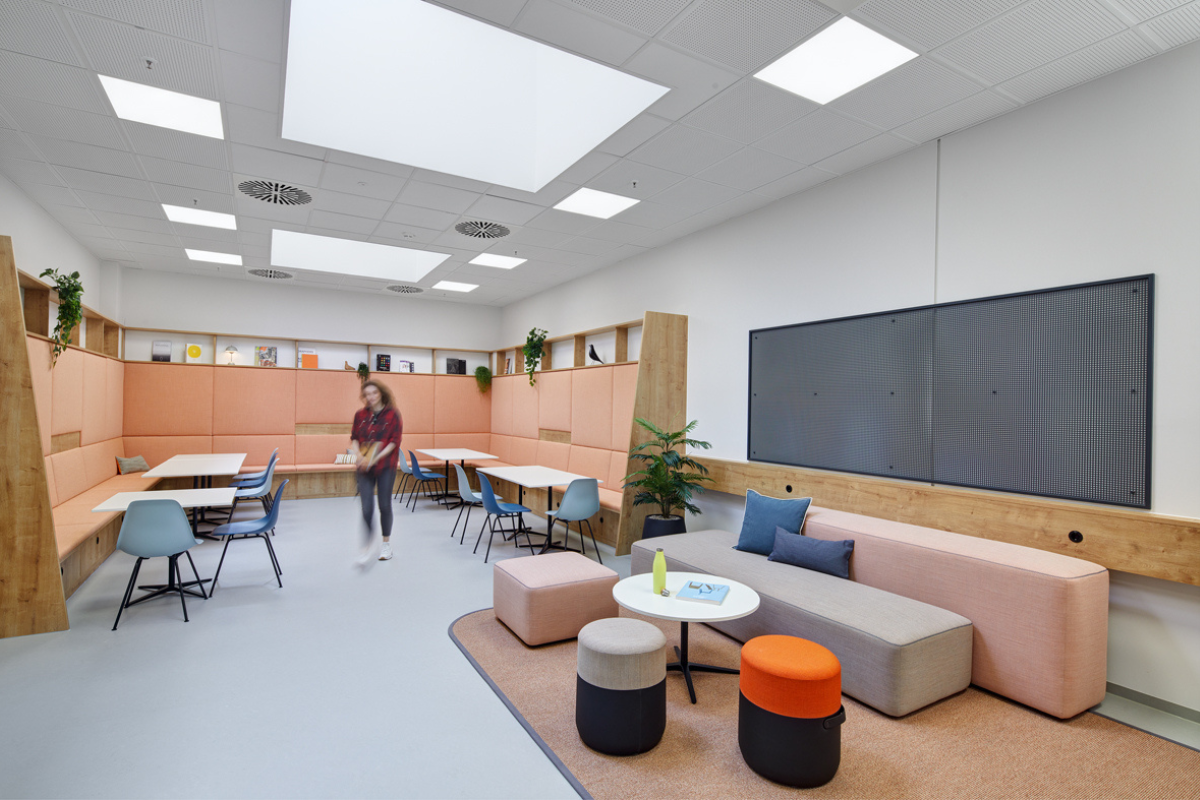 Blick in ein von designfunktion gestaltetes Buero, in dem Tische und Sofas stehen und eine Person durch das Bild geht