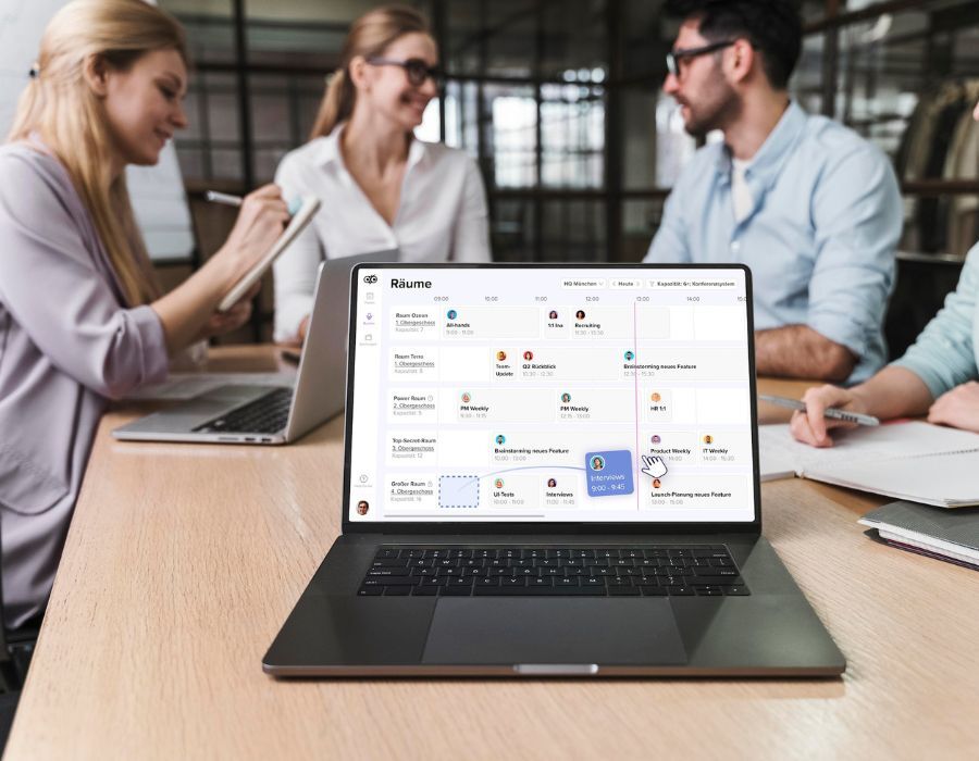 Menschen in Meetingsituation mit Laptop, auf dem das Workplace-Management-System deskbird zu sehen ist