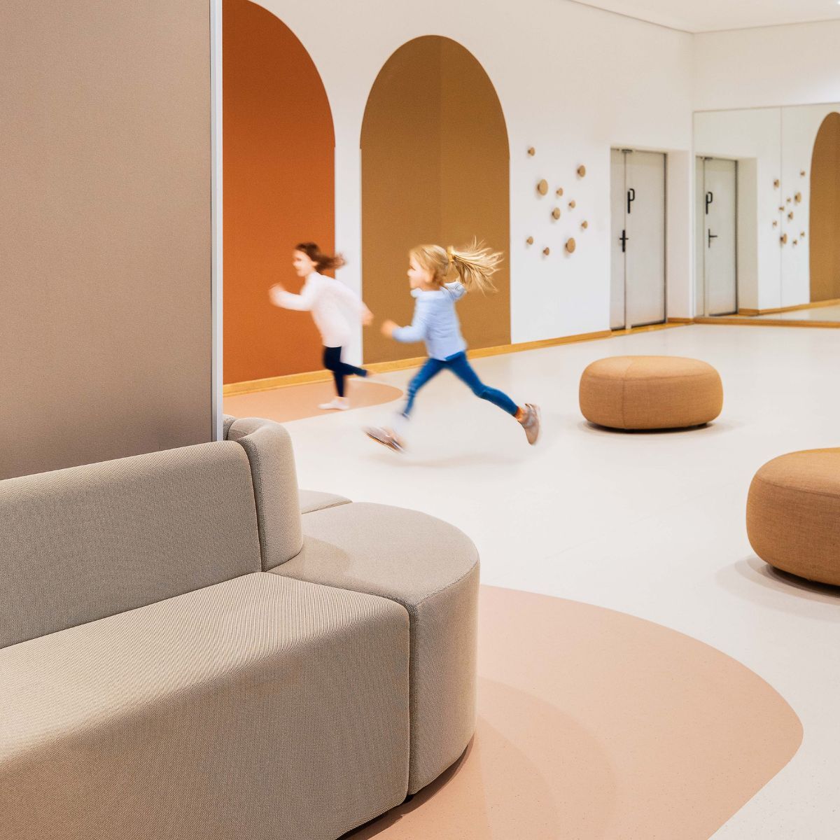 um die Ecke laufende Sitzbank und spielende Kinder im Gemeinschaftsraums der Frankfurt International Primary School in Oberursel, geplant und eingerichtet von designfunktion