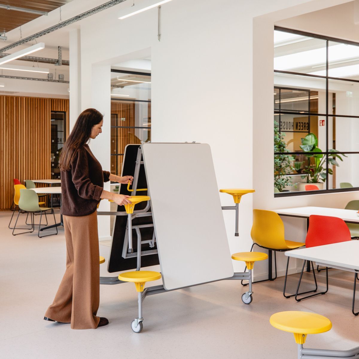 Frau klappt mobiles Möbel zusammen, in der Cafeteria der Frankfurt International School, geplant und eingerichtet von designfunktion