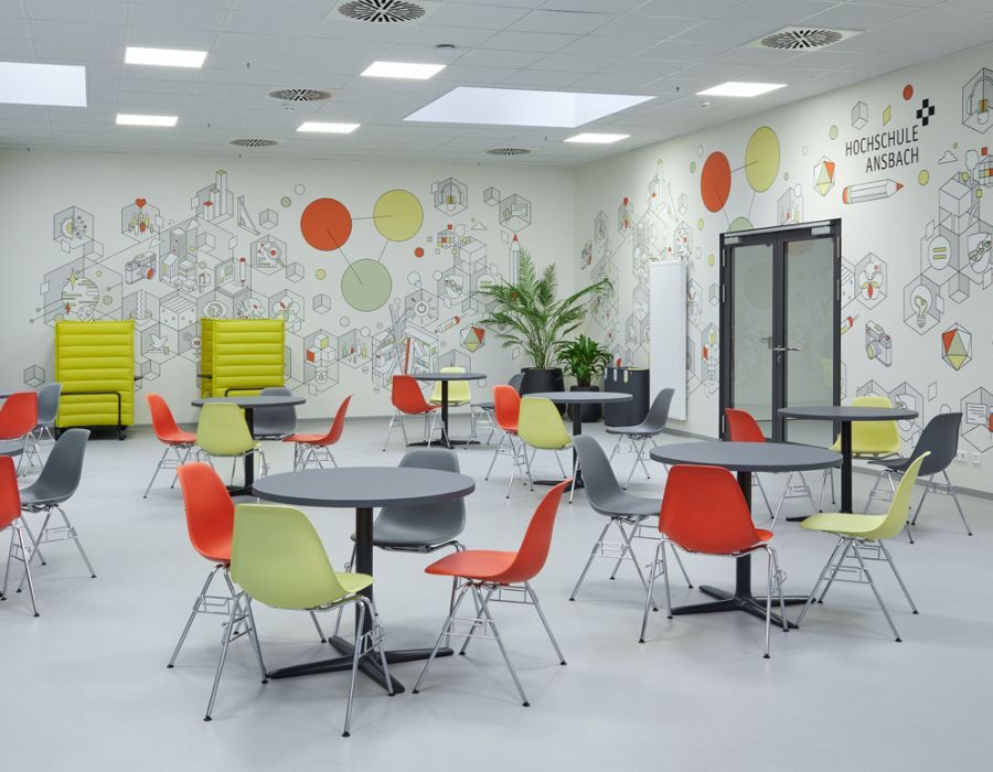 Gemeinschaftsbereich mit Stühlen, Tischen und individuellem Wandbild der Hochschule für angewandte Wissenschaft Ansbach, geplant und eingerichtet von designfunktion