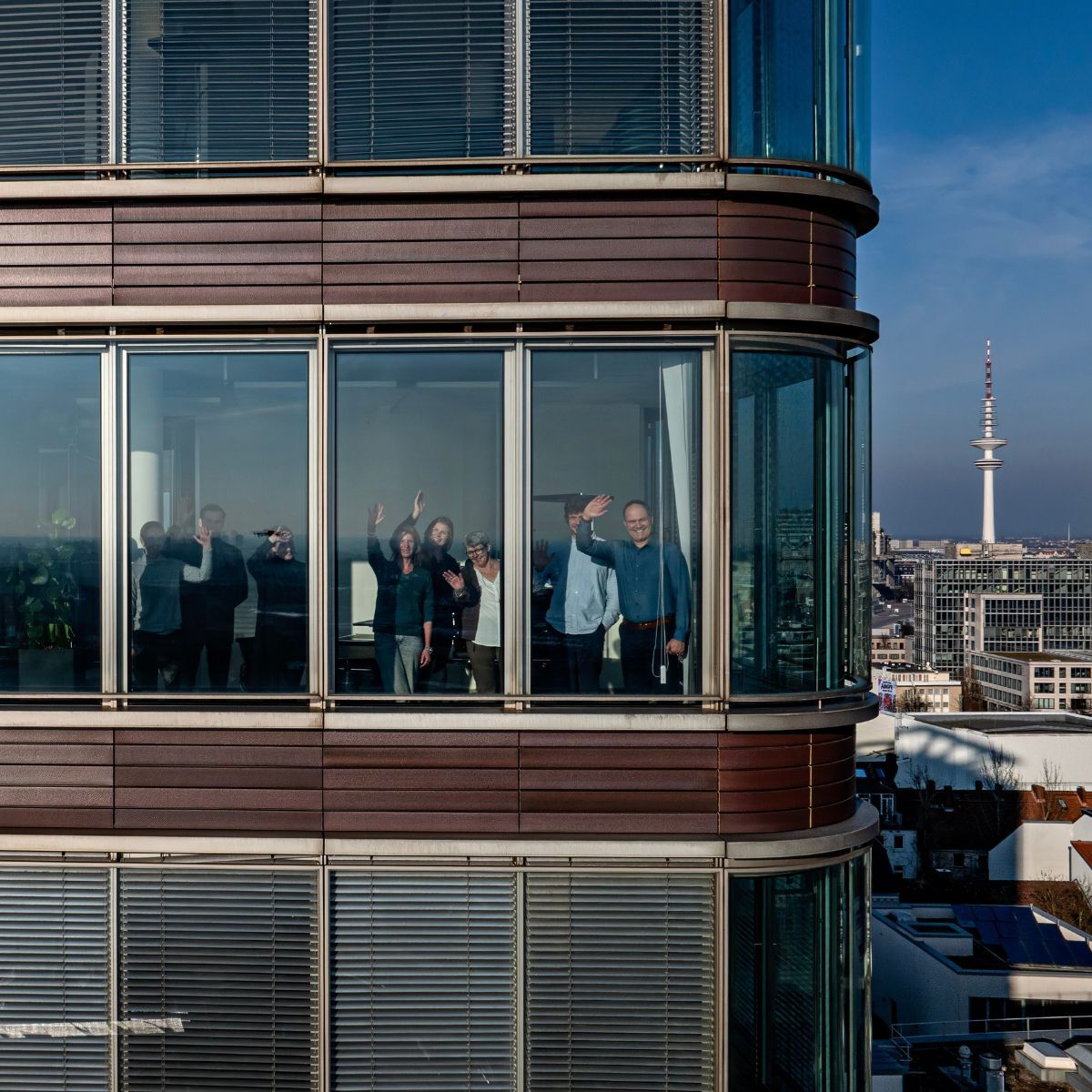 Mitarbeitende winken durch die Glasscheibe